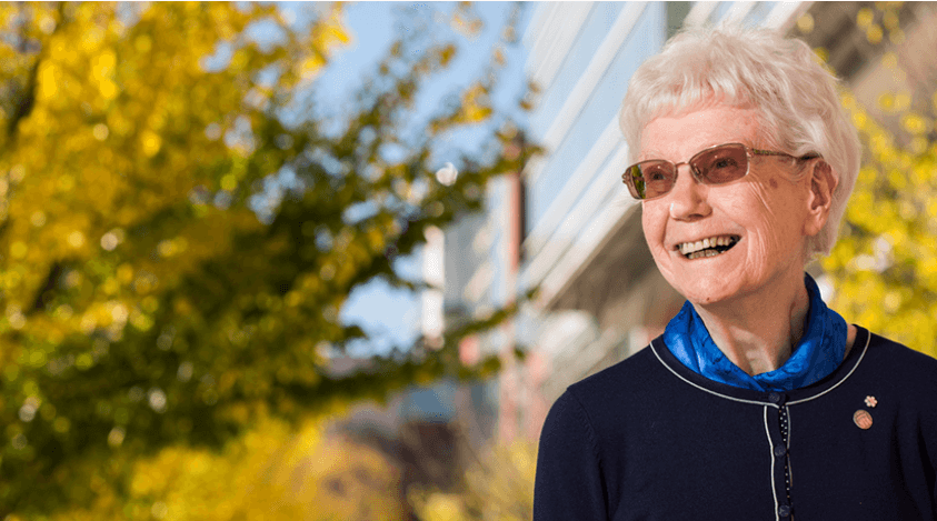 A wide shot of Margaret-Ann Armour standing in front of yellow, autumnal trees in front of CCIS.