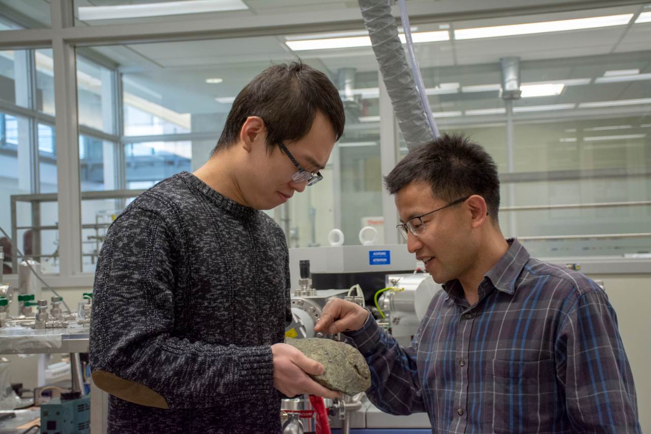 PhD student Kan Li (left) and Long Li (right) examine a basaltic pillow lava sample from the top part of igneous oceanic crust.