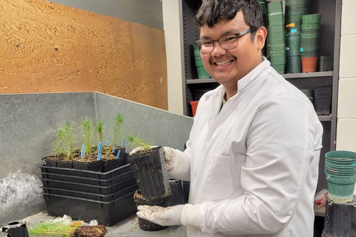 ISTEAM student intern Bo Ragot, pictured holding a plant in a greenhouse facility.